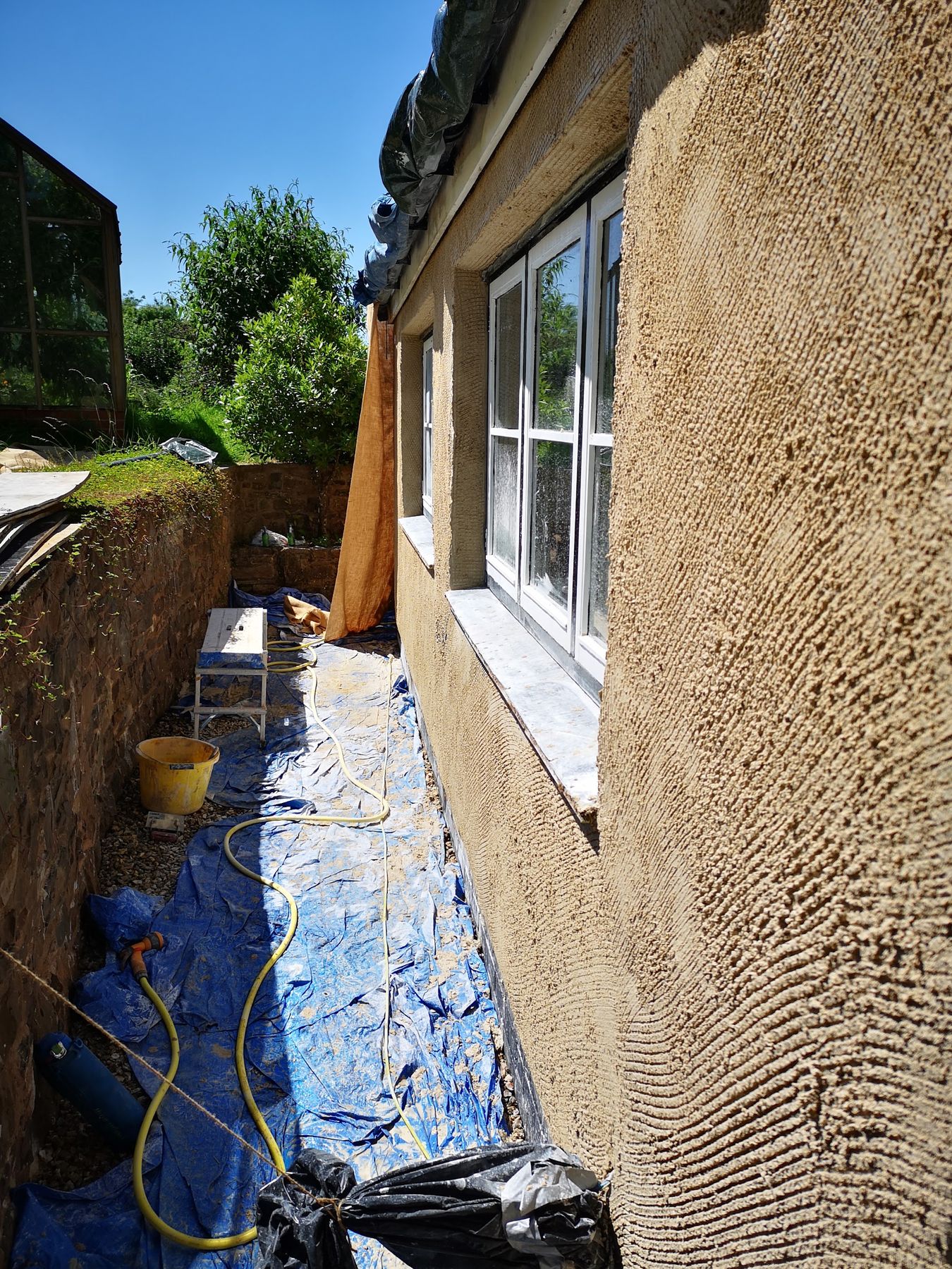 An exterior wall with a fresh coat of render, dust sheets laid along the path